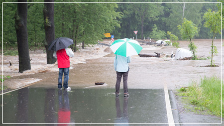 Zwei Personen mit Regenschirm auf einer Straße, die überflutet ist