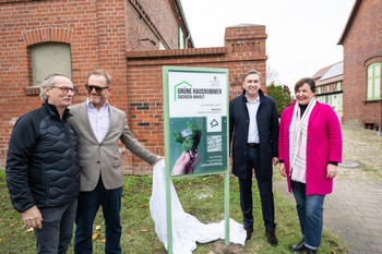 Großes Schild mit der Aufschrift „Grüne Hausnummer“  vor dem Vierseitenhof