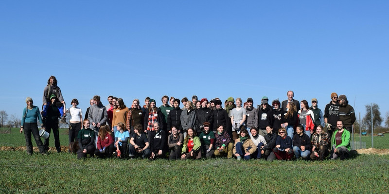 Landesaktionstag des FÖJ Gruppenbild der 40 FÖJ-Teilnehmenden, alle stehen mit Gartengeräten in der Hand auf einer grünen Wiese im Hintergrund blaue Himmel im Ökodorf Sieben Linden